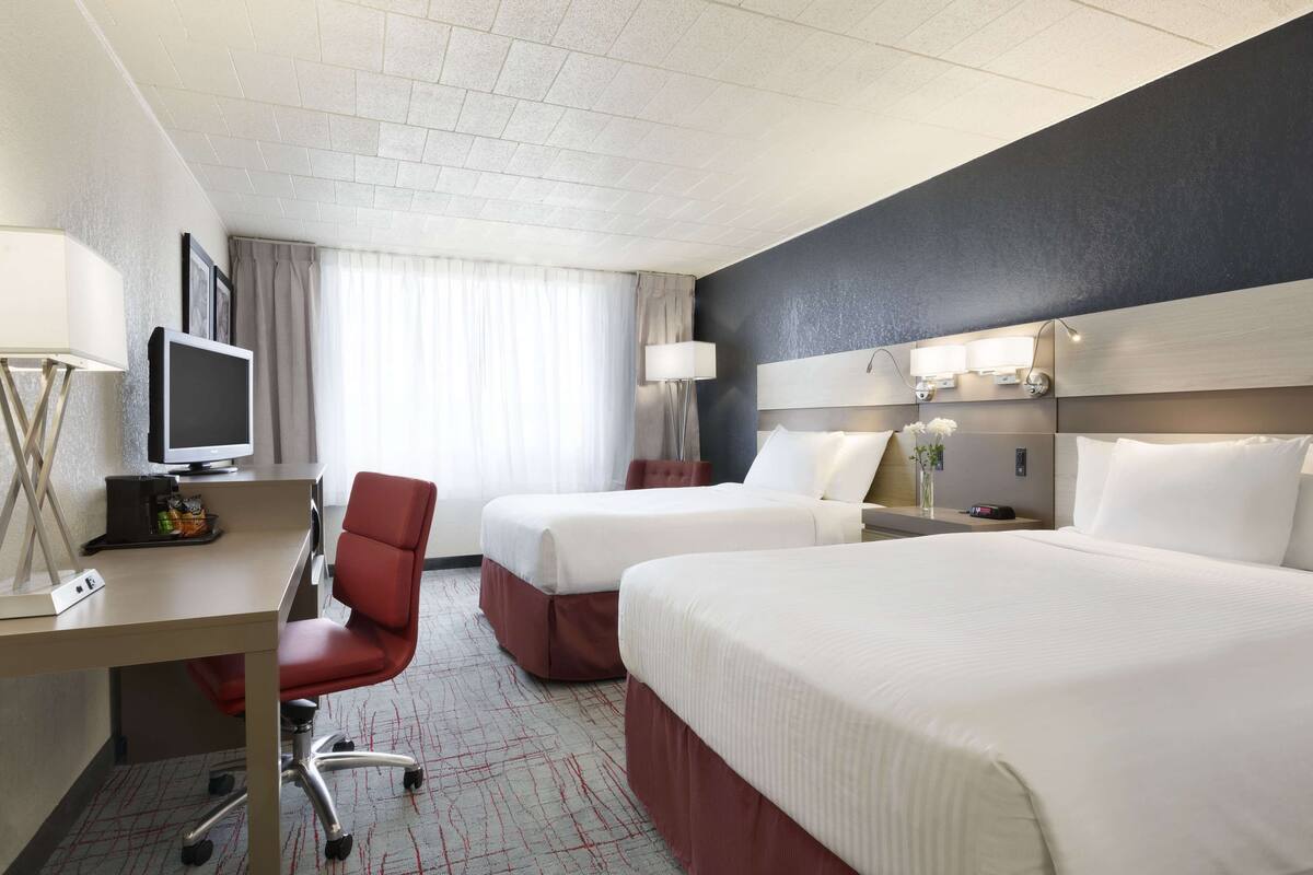 A hotel room with two beds, a desk with a computer, a chair, and a TV.