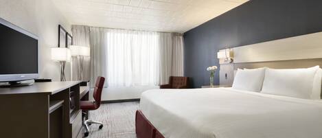 A hotel room with a large bed, a desk, a chair, a television, and a window with curtains.