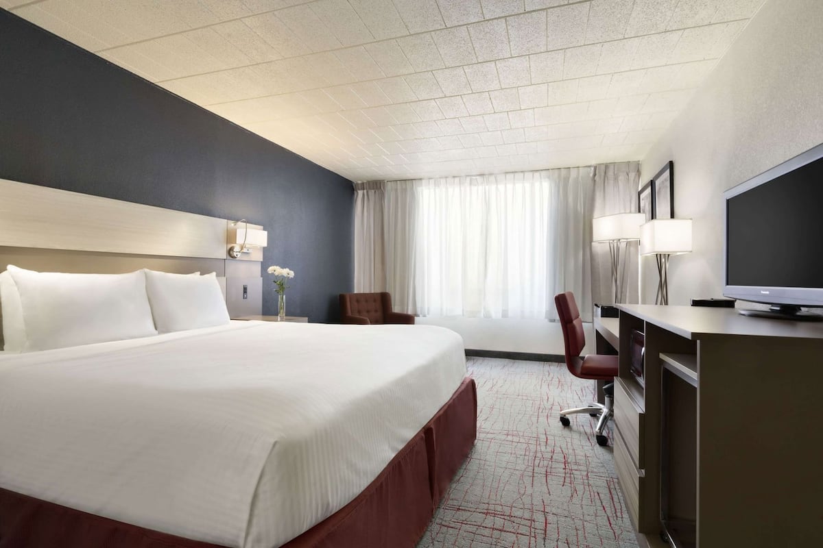 A hotel room with a large bed, a desk with a television, a chair, and a window with curtains.