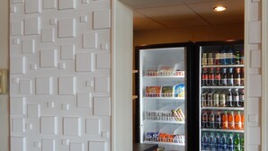 A hallway with a patterned wall and a vending machine stocked with snacks and drinks.