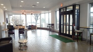 A spacious lobby with a wooden floor, seating areas, and large windows offering views of the outside.