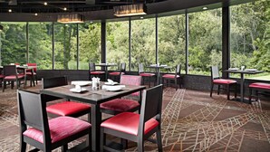 A restaurant with tables and chairs, large windows, and a view of trees.