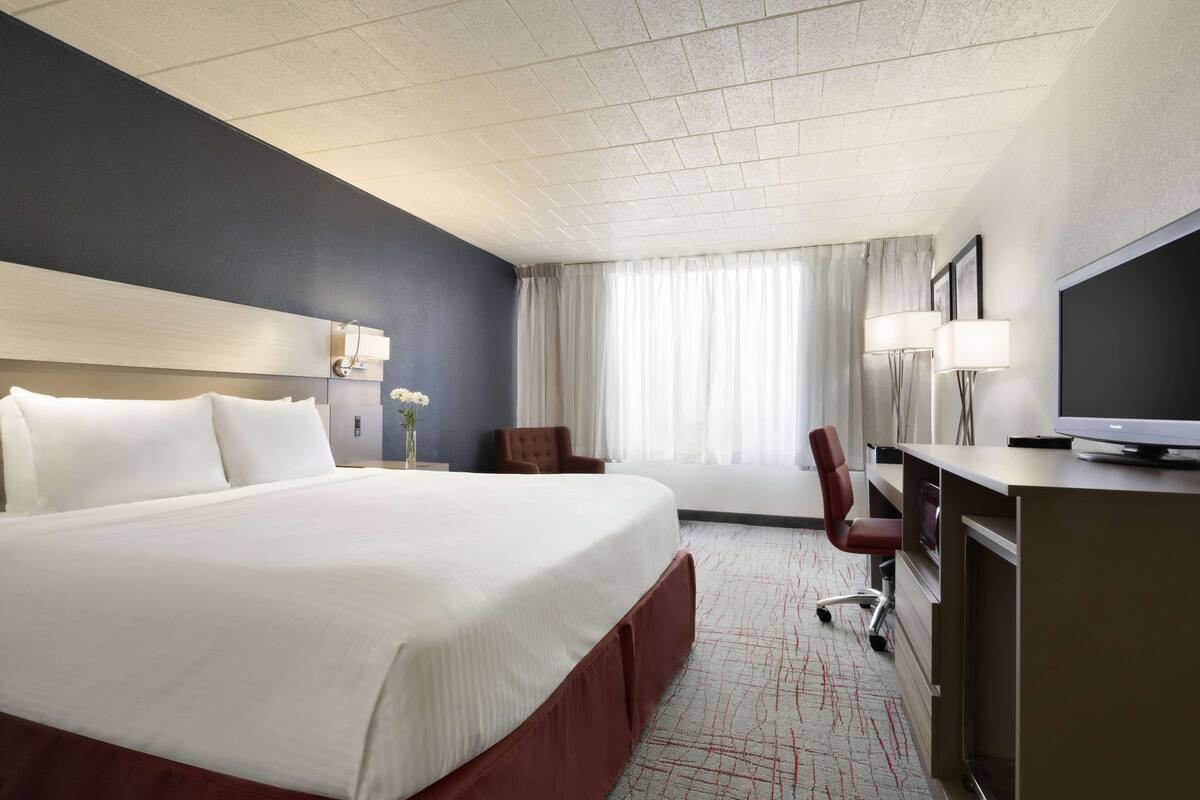 A hotel room with a large bed, a desk with a computer, a chair, and a television.
