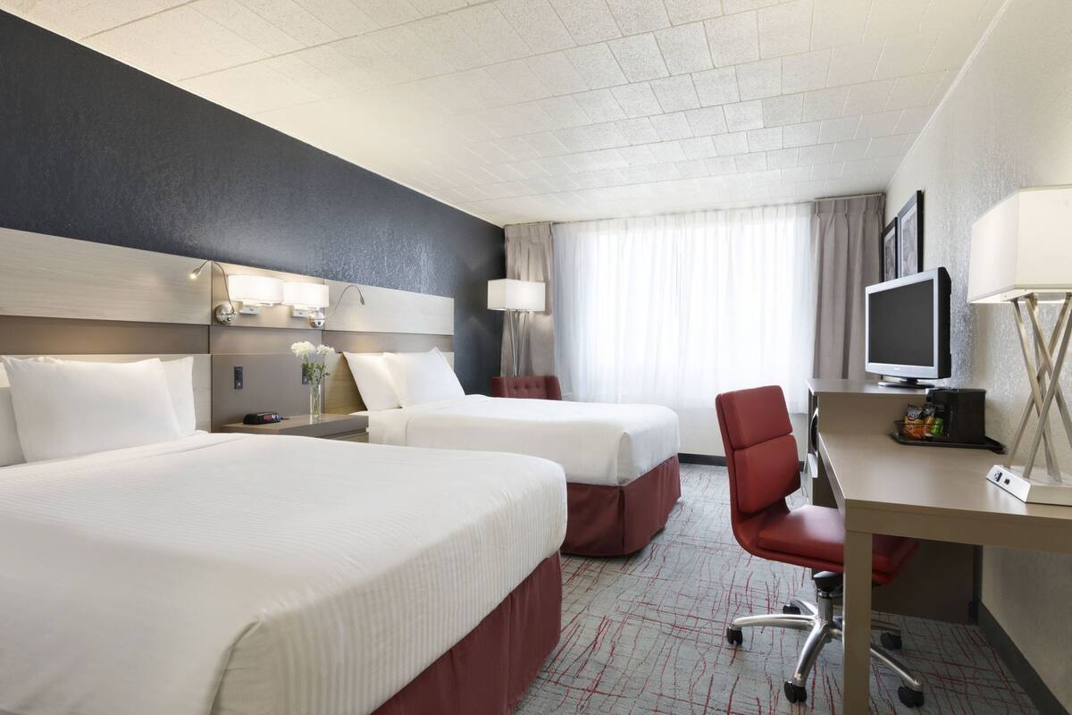 A hotel room with two beds, a desk with a chair, a television, and a window with curtains.