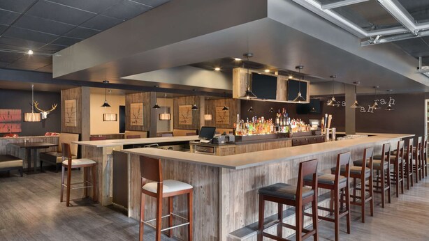 A modern bar area with a long counter, bar stools, and a variety of bottles.