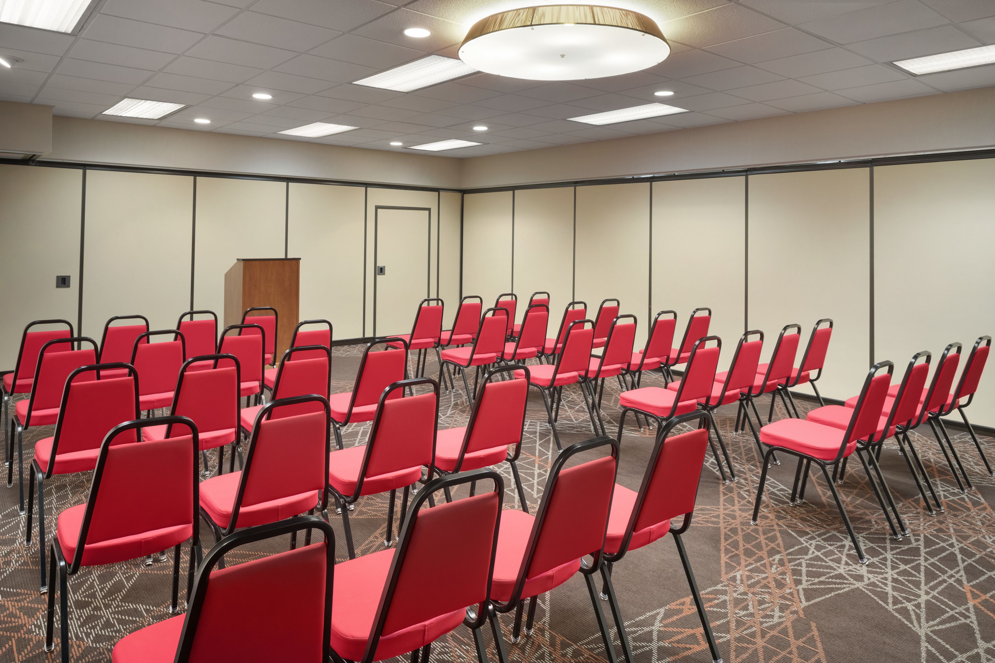 A conference room with rows of red chairs, a podium, and a patterned carpet.