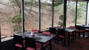 Un ristorante con ampie finestre che si affaccia su alberi e un idrante all'esterno. I tavoli sono disposti con sedie imbottite rosse.