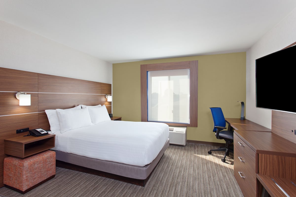 A hotel room with a bed, a desk, a chair, a TV, a window, and a nightstand.