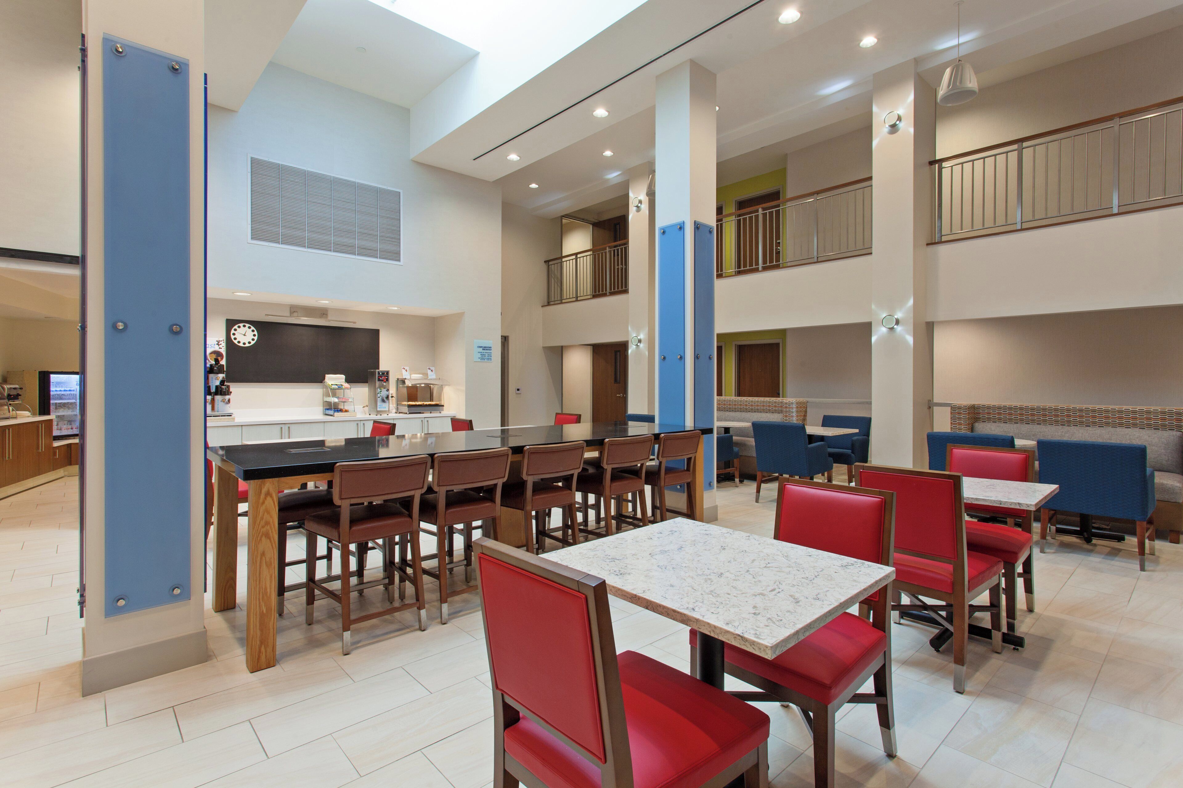 A modern dining area with multiple tables and chairs, a kitchen in the background, and a balcony with railings.