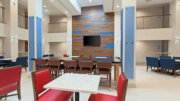 A modern dining area with a central table, red and blue chairs, and a flat-screen TV mounted on a wooden wall.