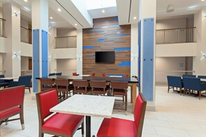 A modern dining area with a central table, red and blue chairs, and a flat-screen TV mounted on a wooden wall. - Holiday Inn Express West Los Angeles by IHG (Los Angeles)