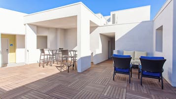 An outdoor patio area with a wooden deck, wicker furniture, and a white building structure.