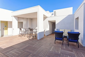 An outdoor patio area with a wooden deck, wicker furniture, and a white building structure. - Holiday Inn Express West Los Angeles by IHG (Los Angeles)