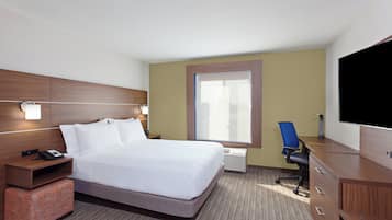 Quarto de hotel com cama, escrivaninha, cadeira, televisão e janela.