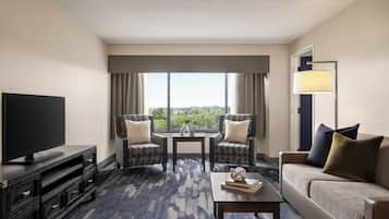 A hotel room with a flat-screen TV, two armchairs, a sofa, a coffee table, and a large window with a view.