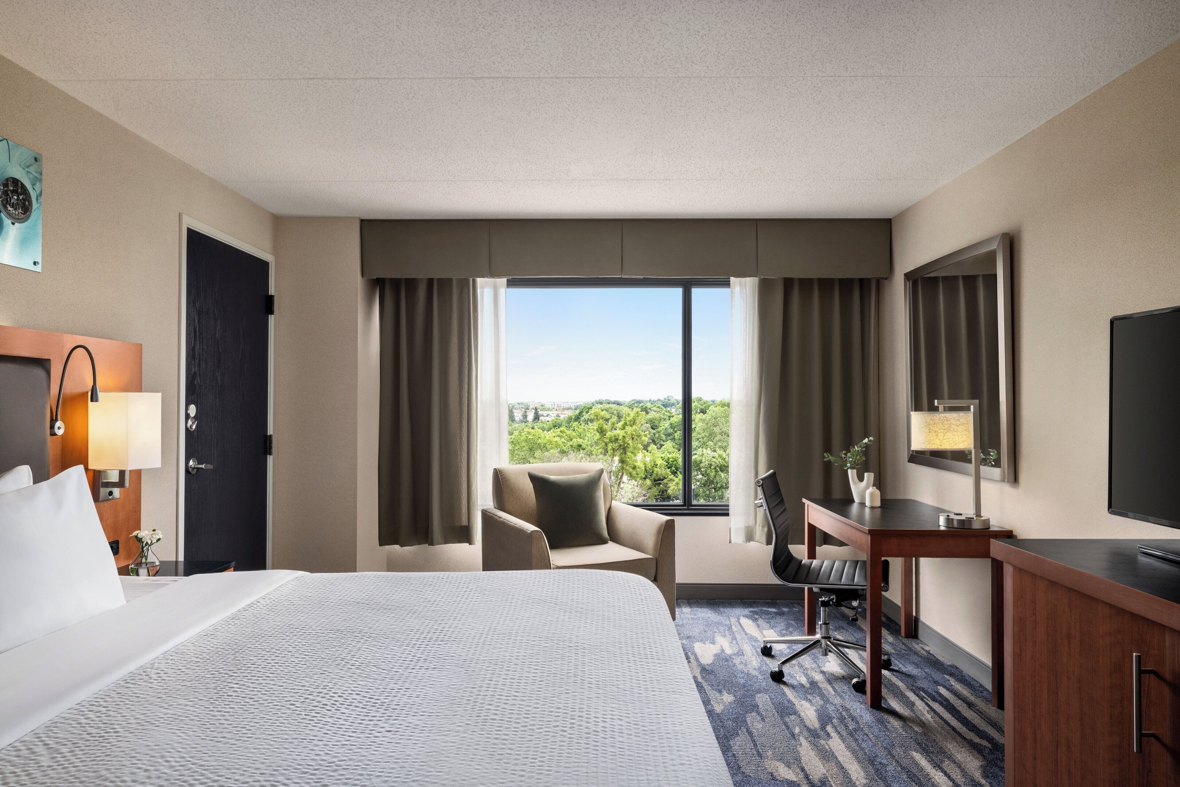 Habitación de hotel con una cama grande, un escritorio, una silla y vistas al exterior.