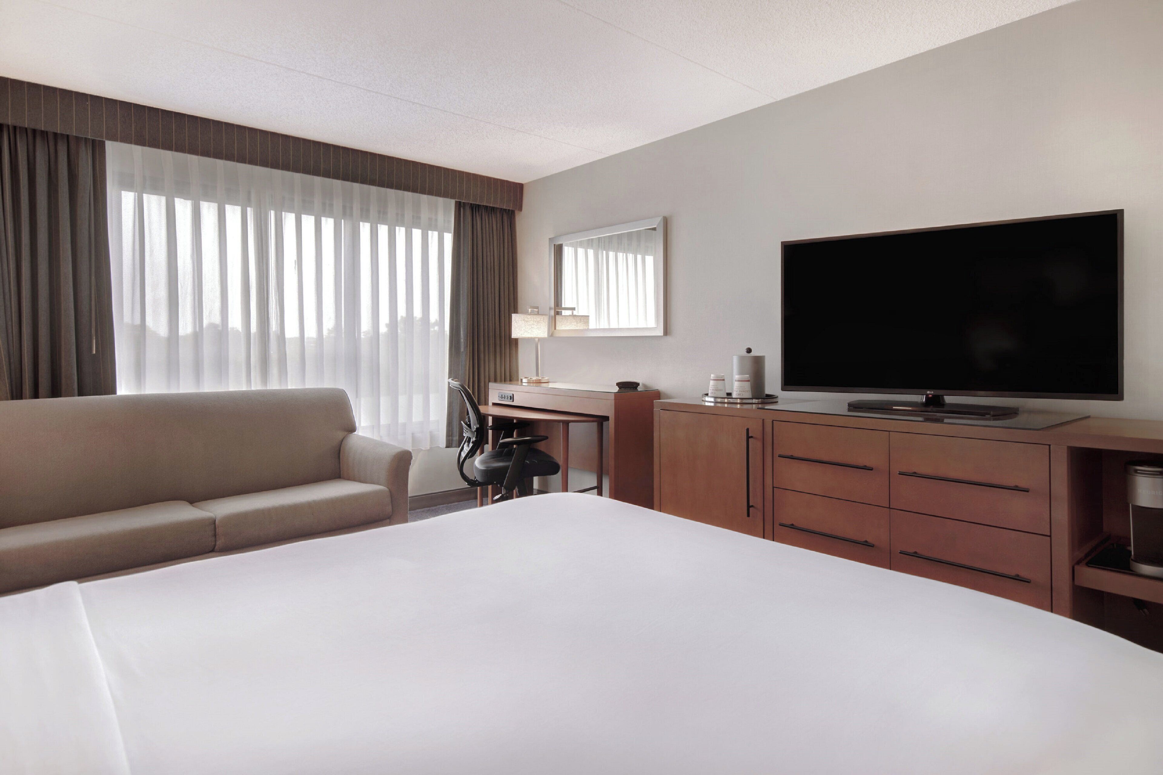 Ein Hotelzimmer mit einem großen Bett, einer Couch, einem Schreibtisch mit Flachbildfernseher und einem Schrank.