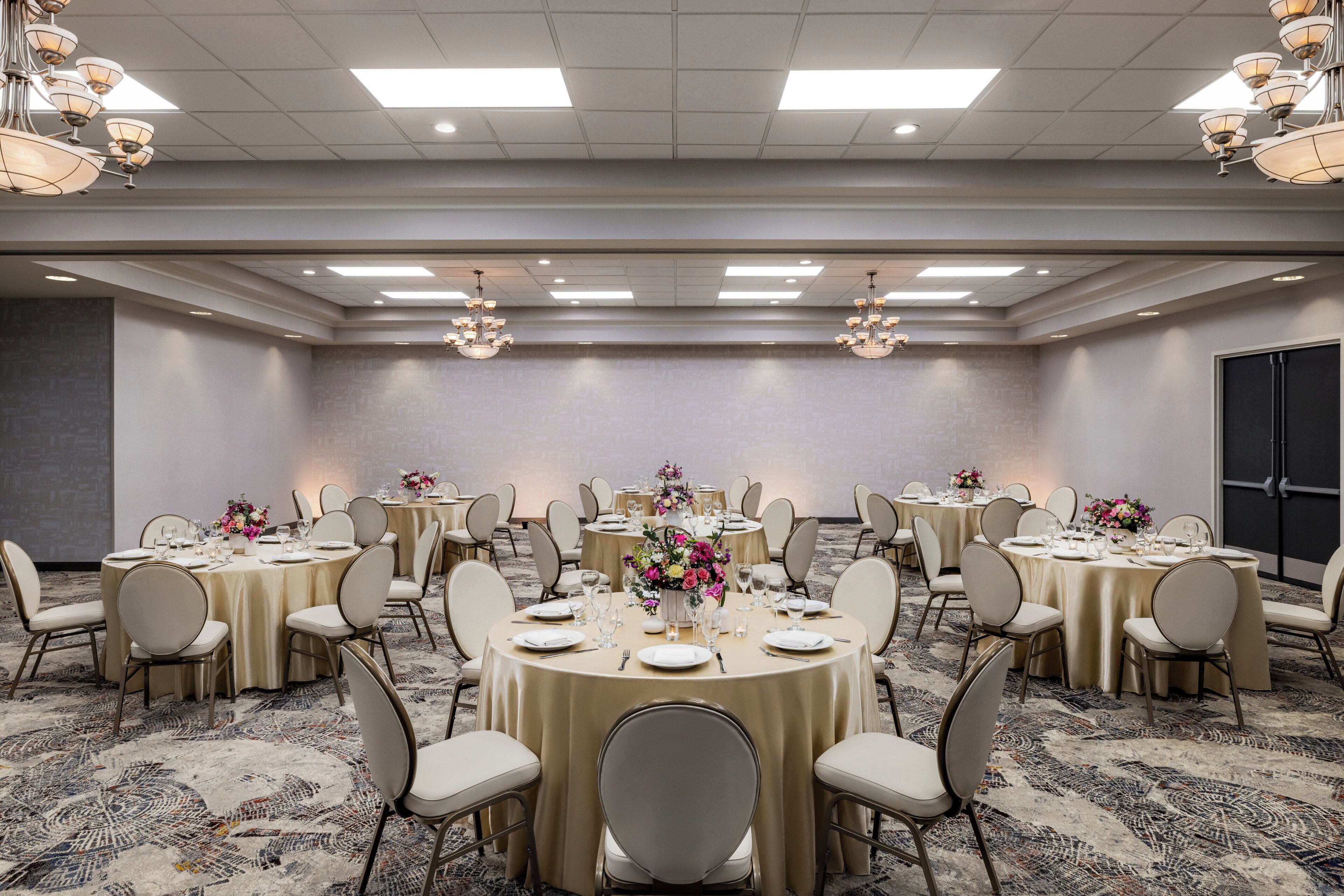 A banquet hall with round tables, chairs, and chandeliers.