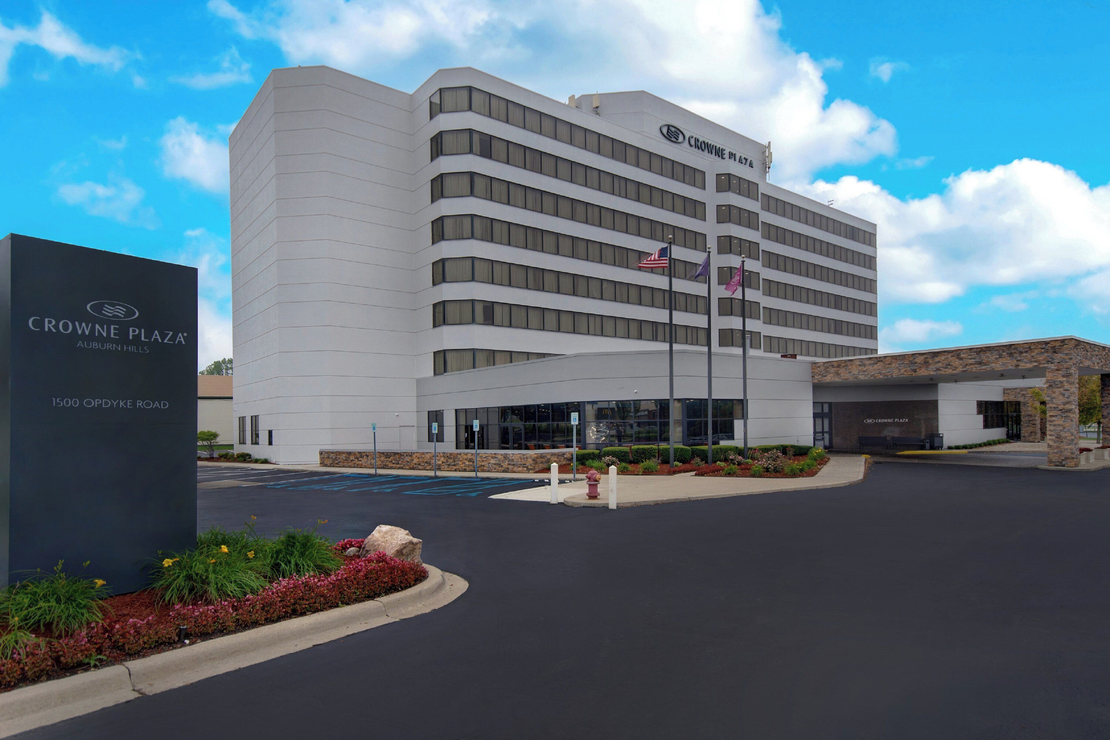 A modern hotel with a prominent entrance, a parking lot, and a landscaped area with flowers and a fire hydrant.