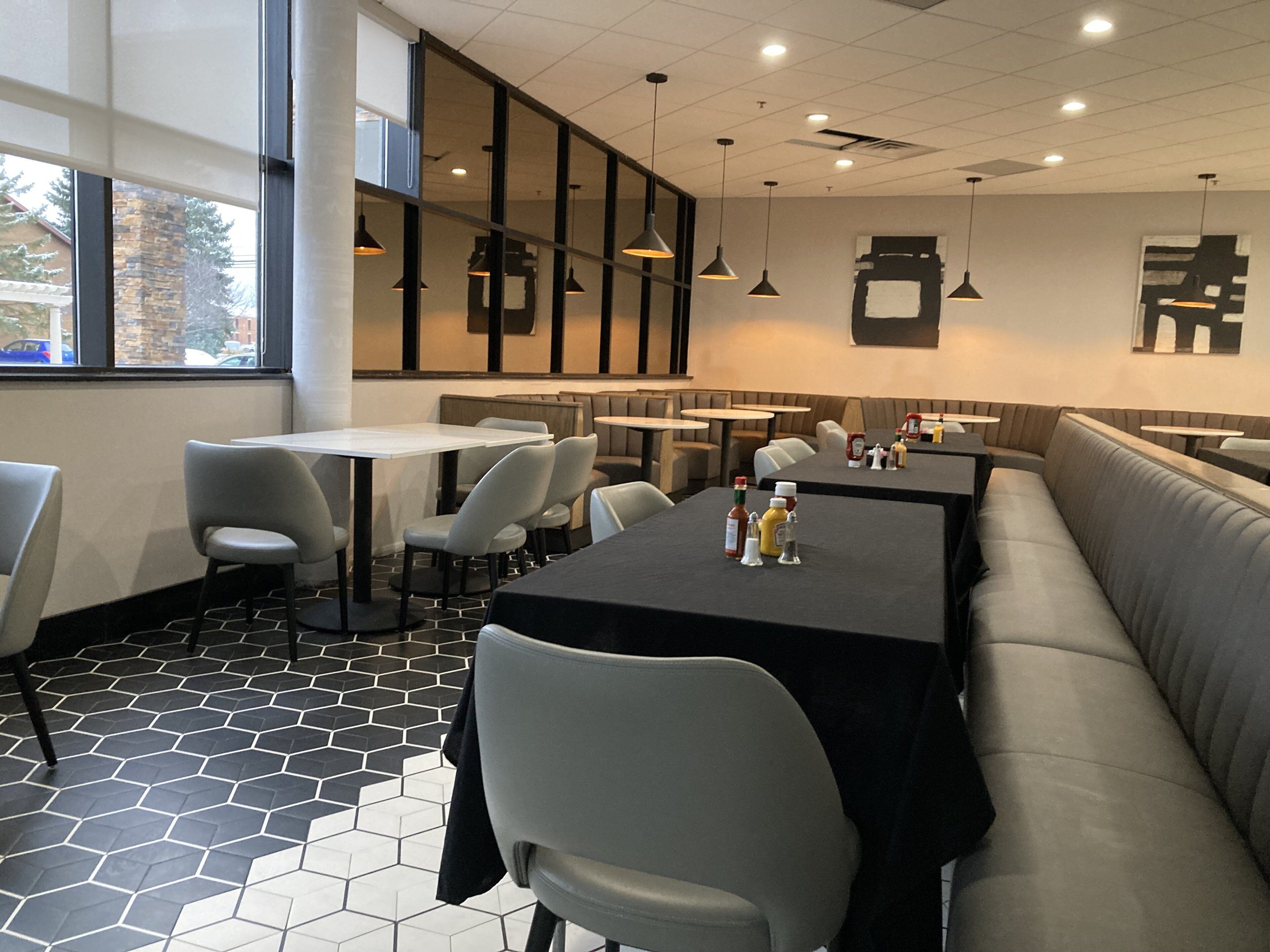 A restaurant with a long counter, multiple tables, and a large window.