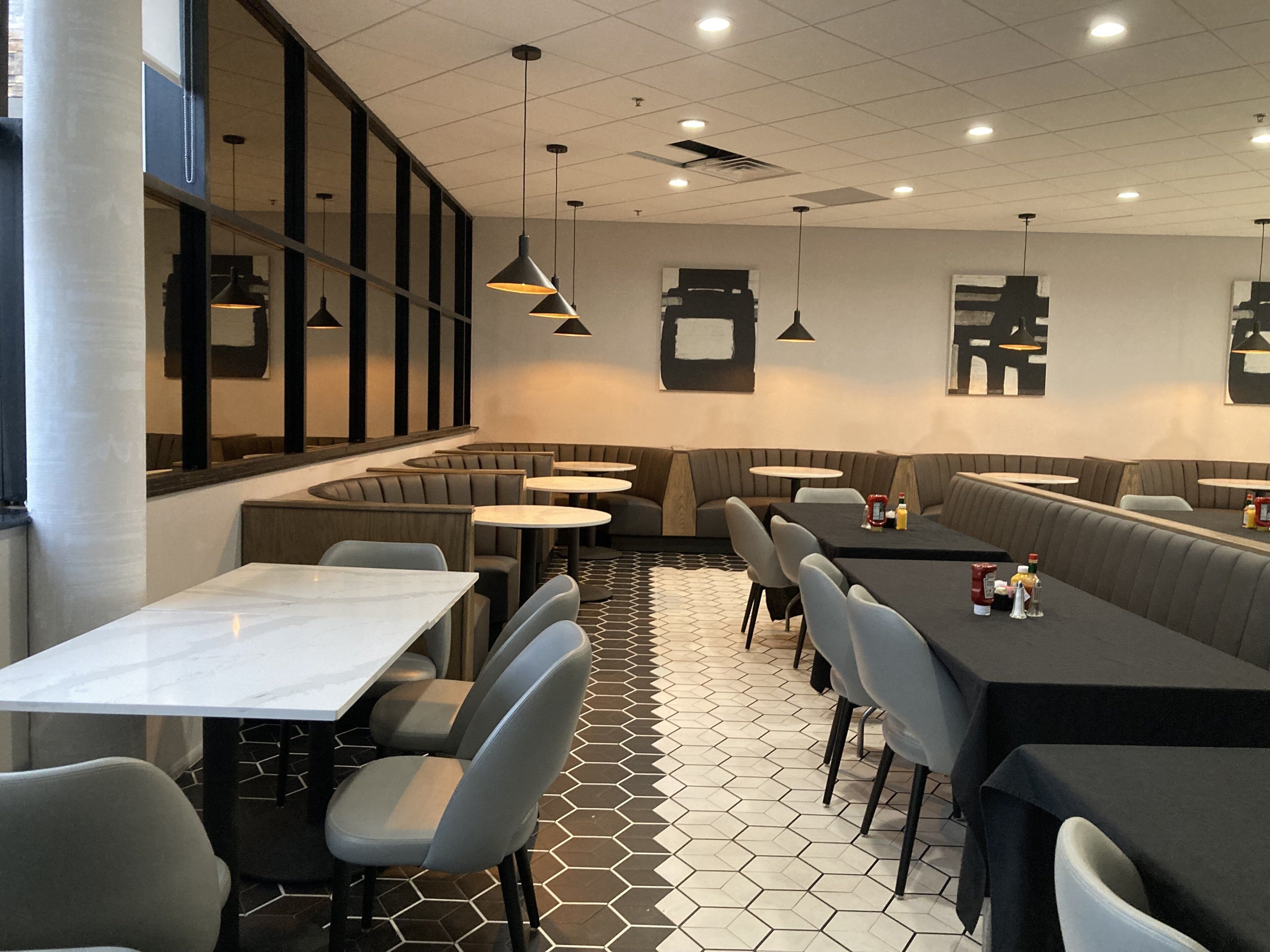 A modern restaurant interior with a long communal table, individual booths, and a patterned floor.