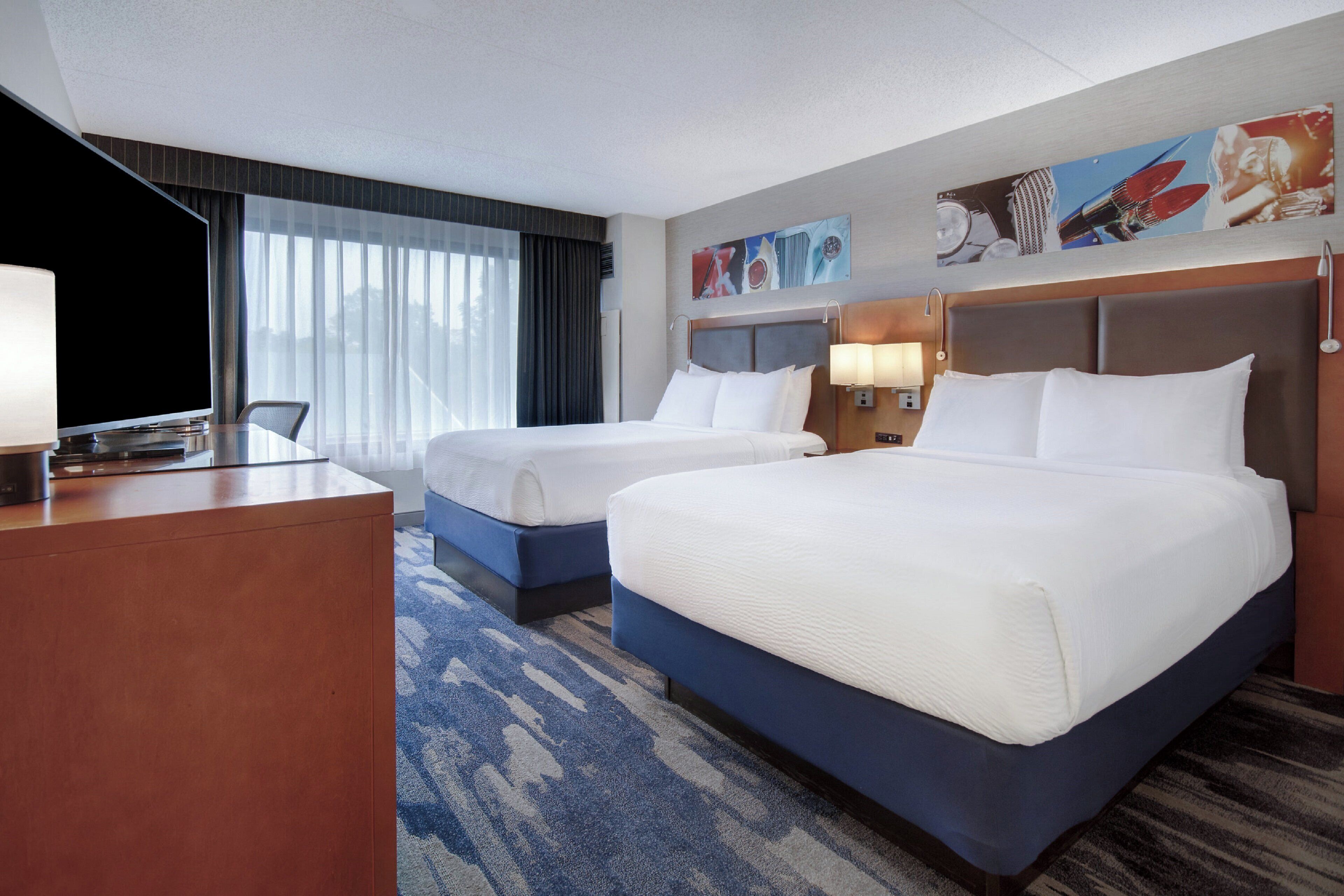 A hotel room with two beds, a desk, and a television.