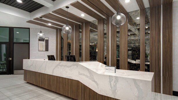 A reception desk with a marble top, wooden paneling, and pendant lighting.