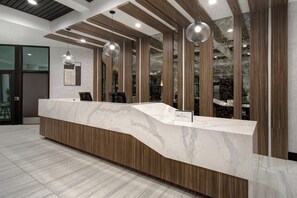 A reception desk with a marble top, wooden paneling, and pendant lighting. - Crowne Plaza Auburn Hills by IHG (Auburn Hills)