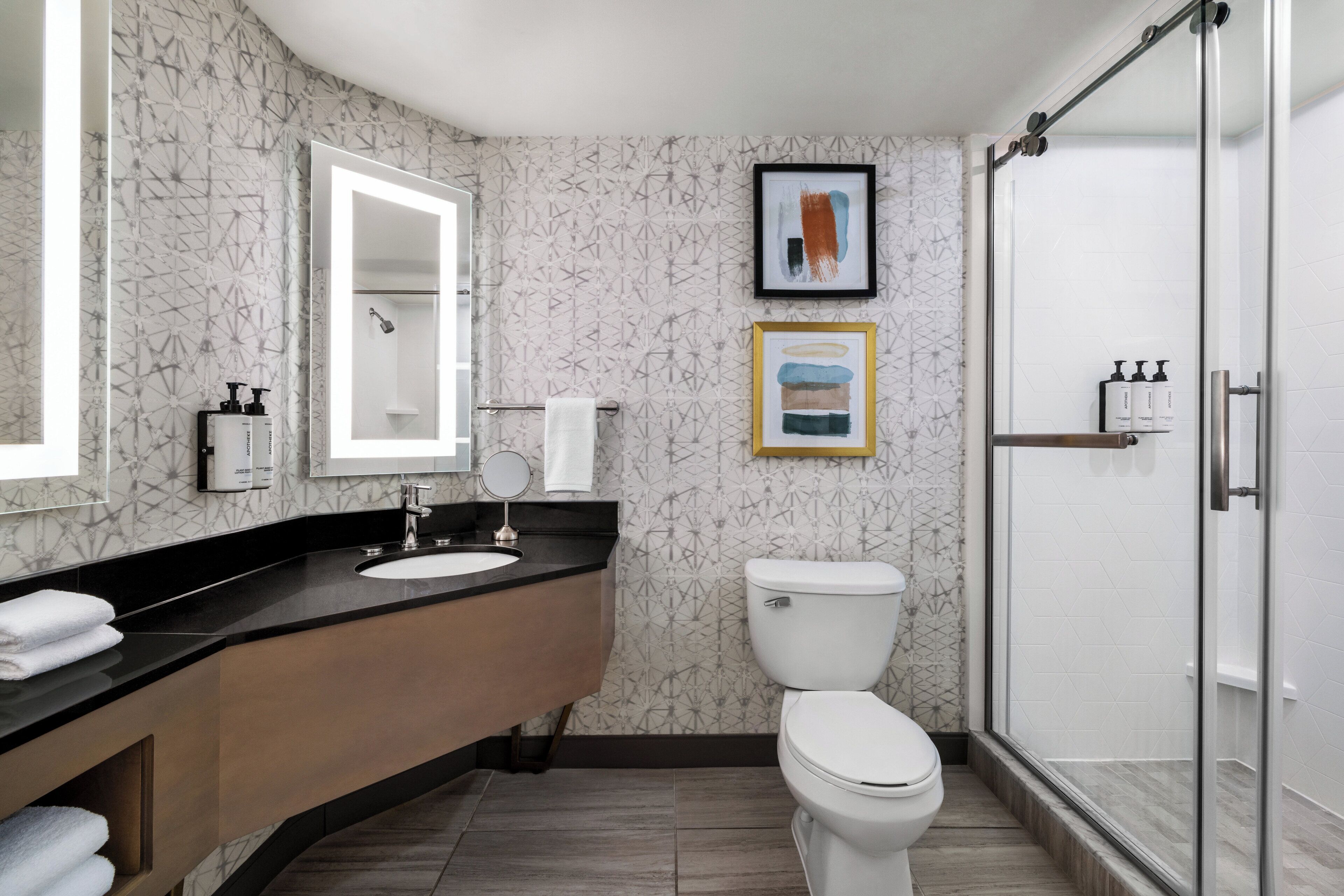Een moderne badkamer met een gebogen wastafel, toilet, een douchecabine van glas en twee kunstwerken in lijsten aan de muur.