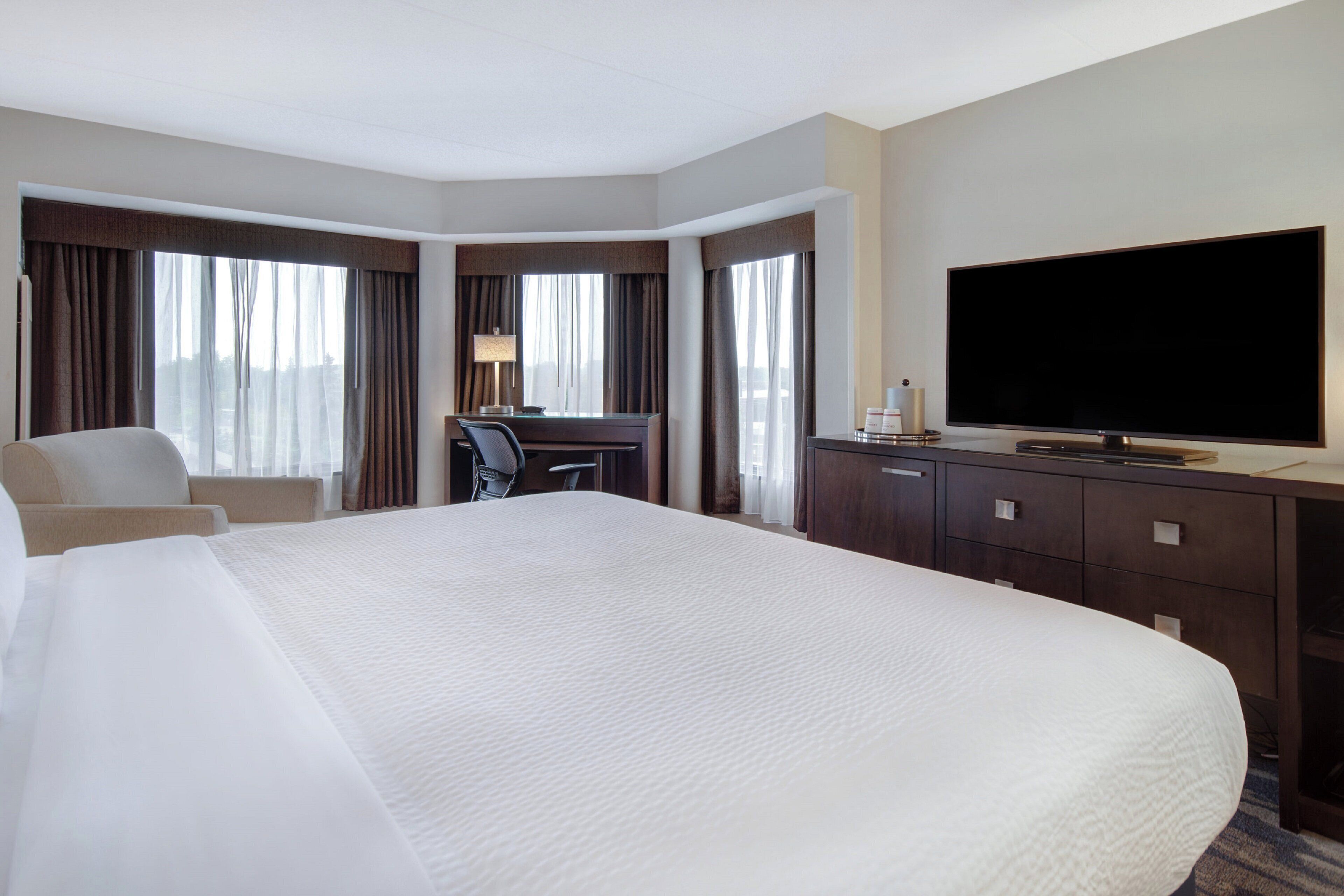 Una habitación de hotel con una cama grande, un escritorio, una silla, un televisor y un armario.