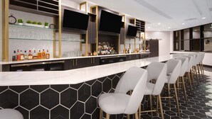 A modern bar area with a long counter, multiple shelves with glassware, and a row of bar stools.