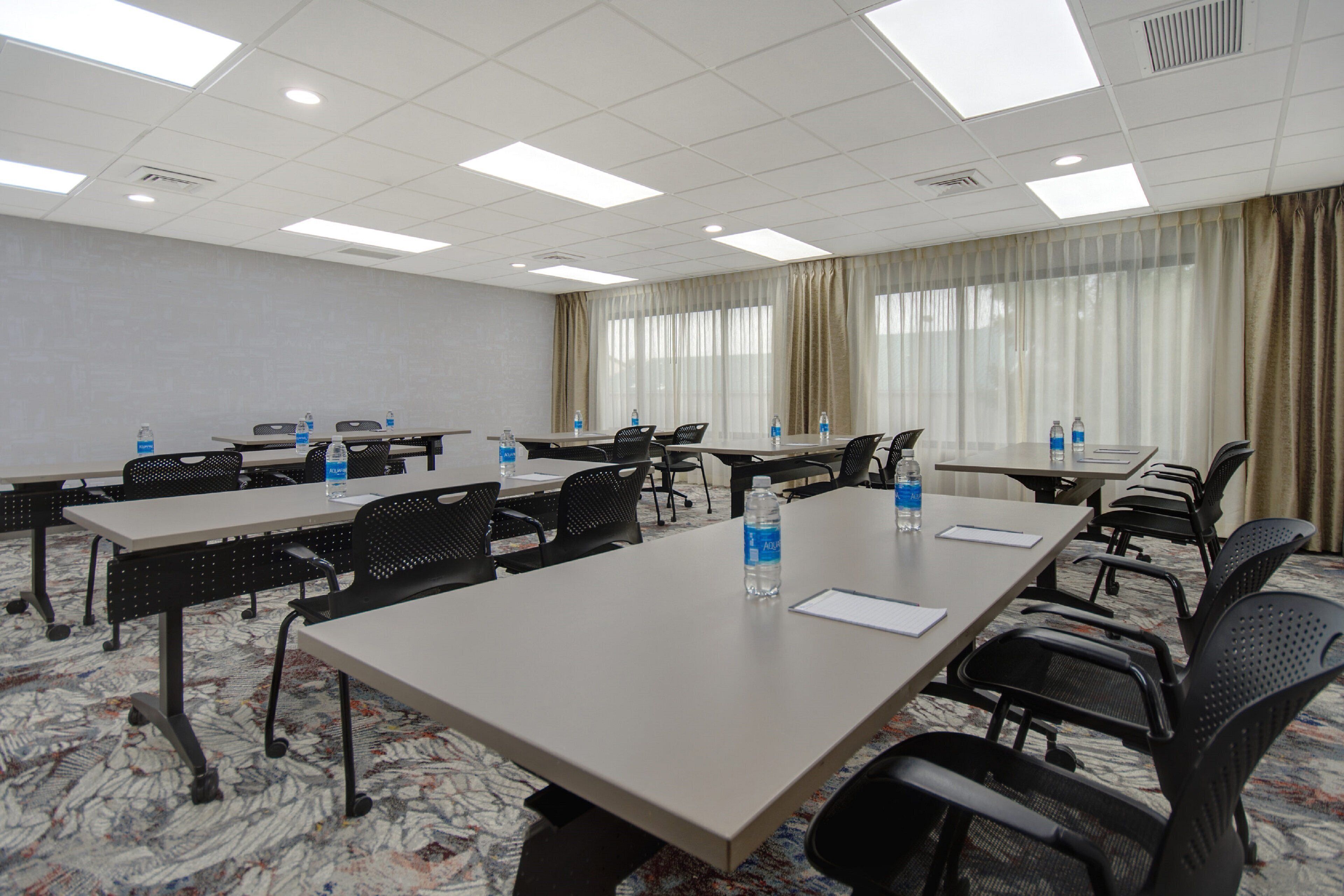 A conference room with multiple tables and chairs, equipped with water bottles and papers.