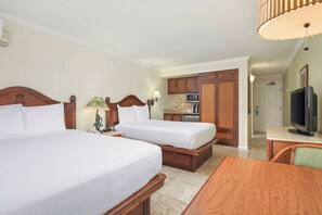 A hotel room with two beds, a wooden desk, a television, and a kitchenette.