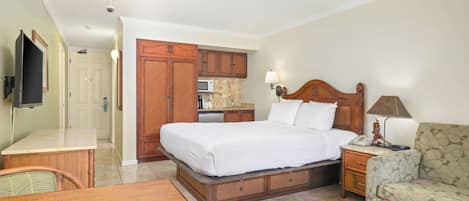 A hotel room with a bed, a desk, a chair, a sofa, a television, a lamp, and a kitchenette.