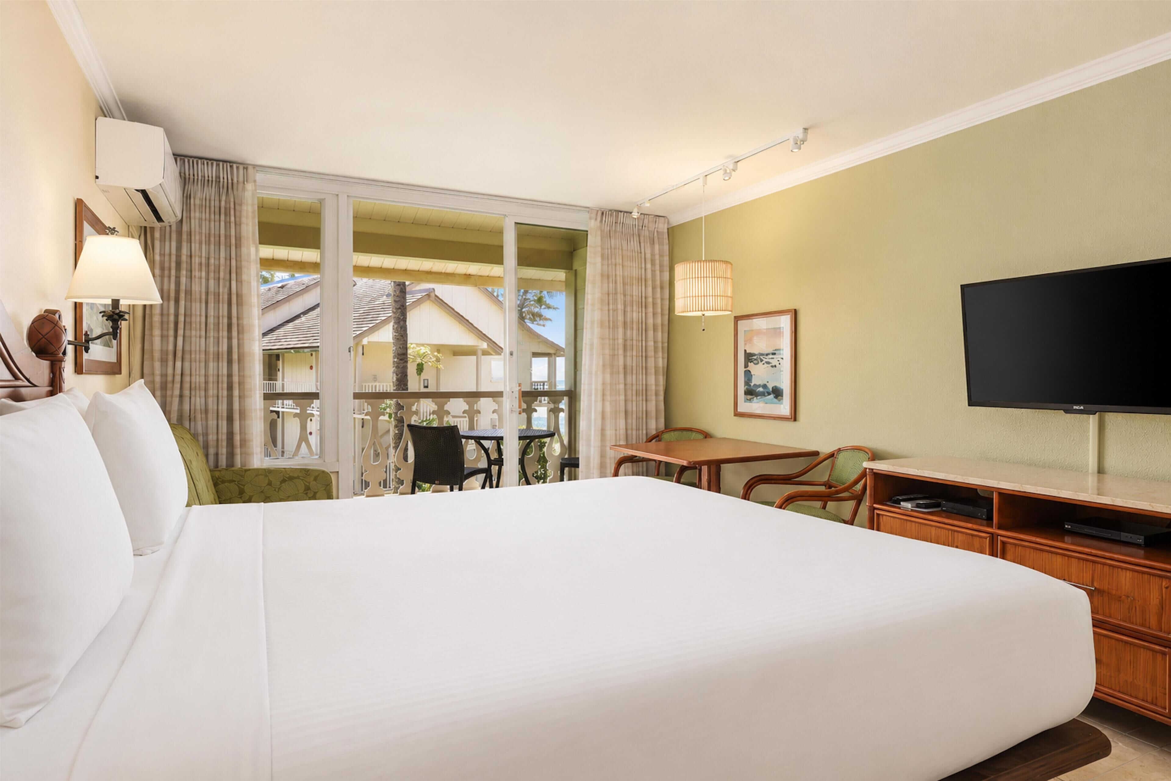 A hotel room with a large bed, a television, a desk with a chair, and a view of the outside.