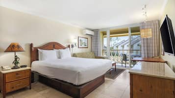 A hotel room with a large bed, a wooden nightstand with a lamp, a desk with a chair, and a TV.