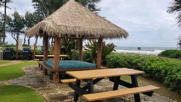 Eine Strandlounge mit Gazebo unter einem Reetdach, Picknicktischen und Blick auf den Ozean.