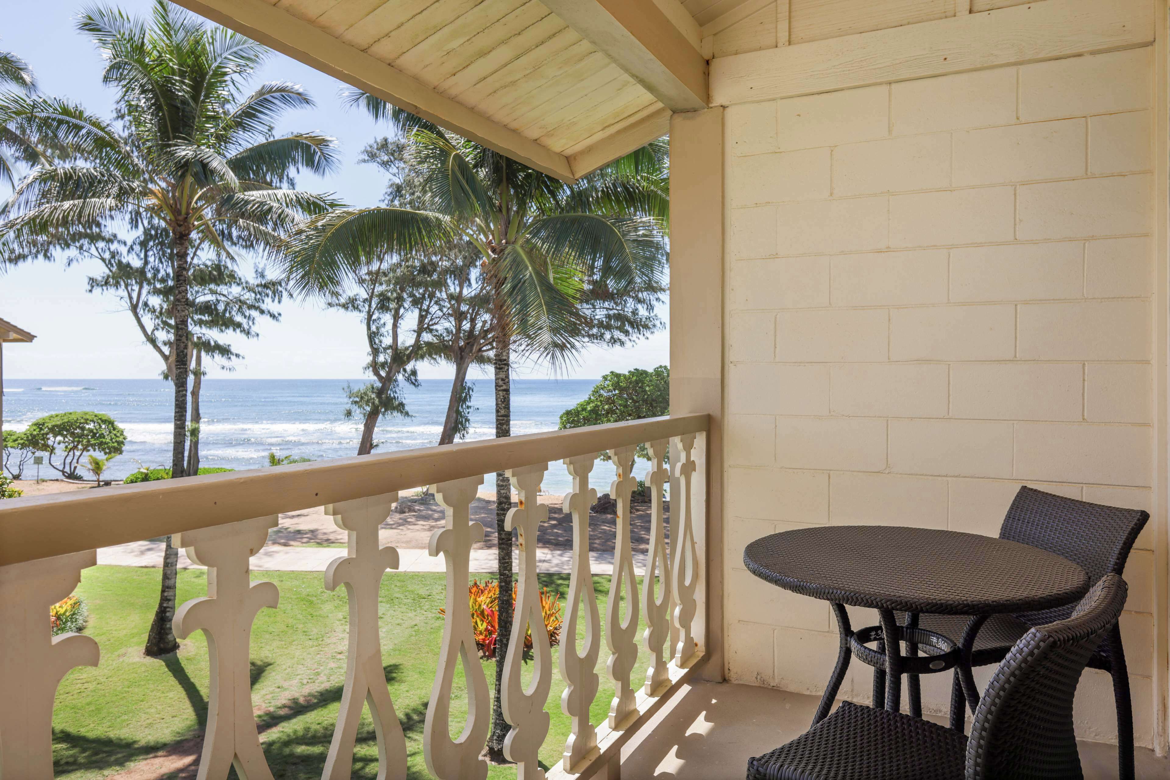 Een balkon met uitzicht op de oceaan, palmbomen en een ronde tafel met stoelen.