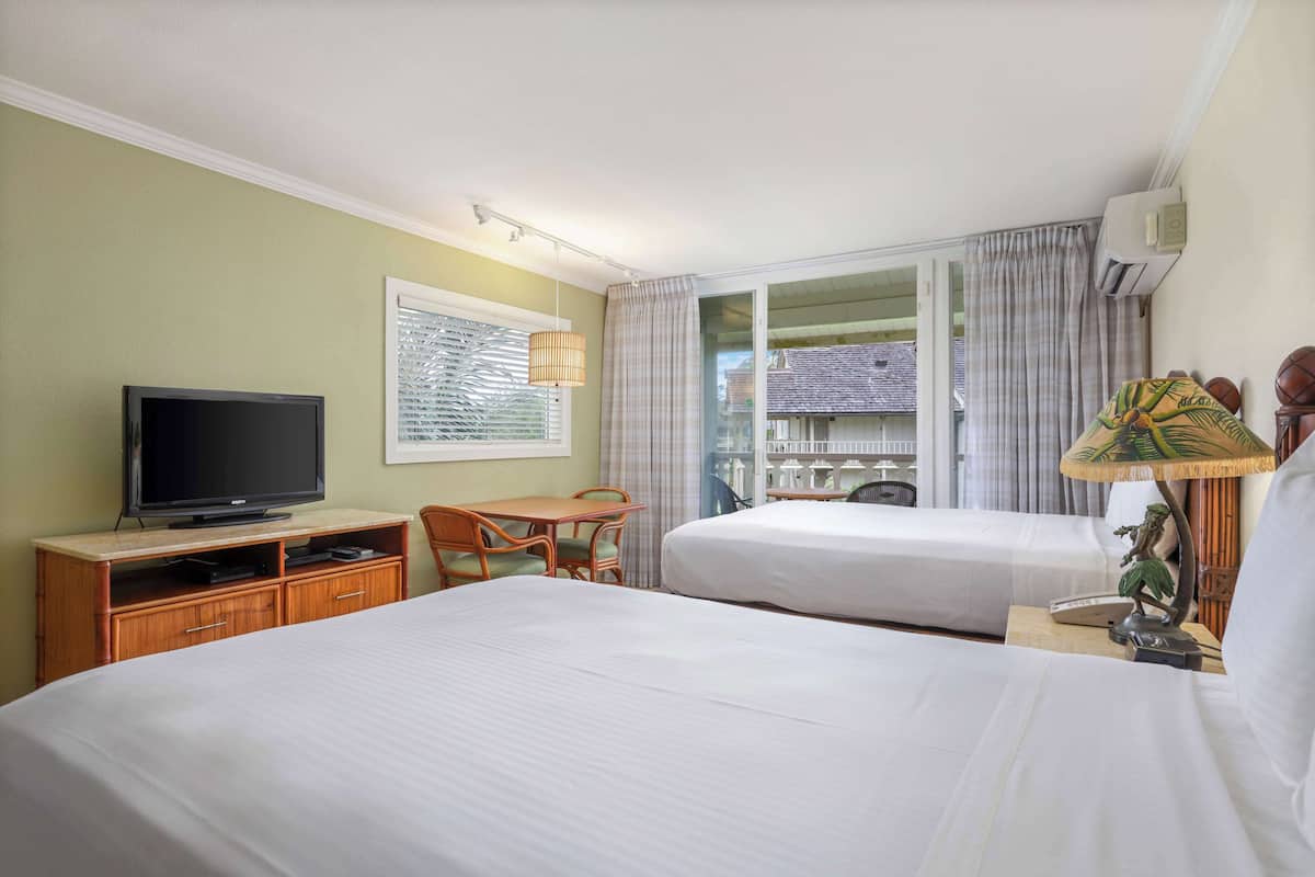 Habitación de hotel con dos camas, televisión, escritorio con silla, lámpara y ventana con cortinas.