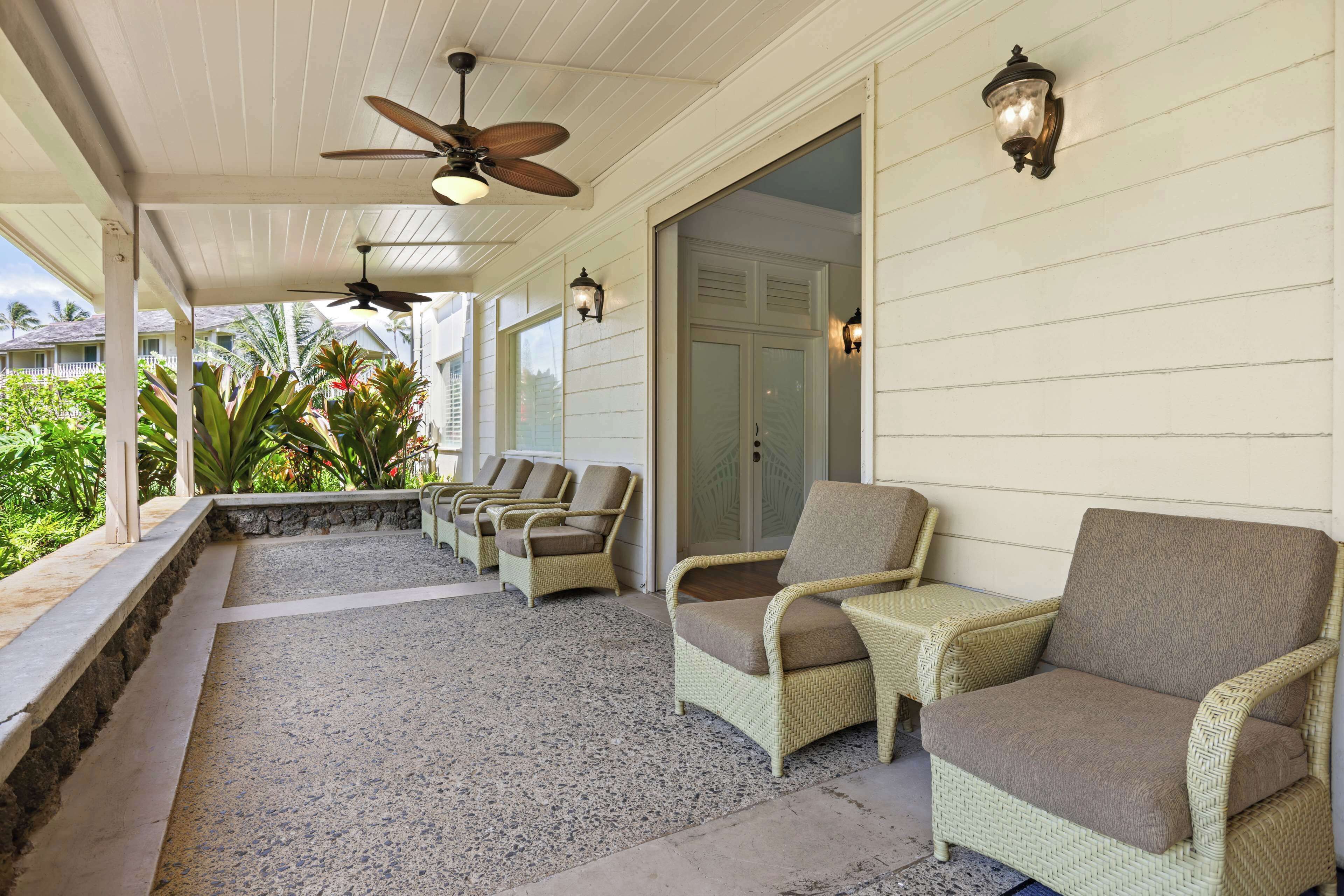 A covered porch with wicker furniture, ceiling fans, and wall-mounted lights.