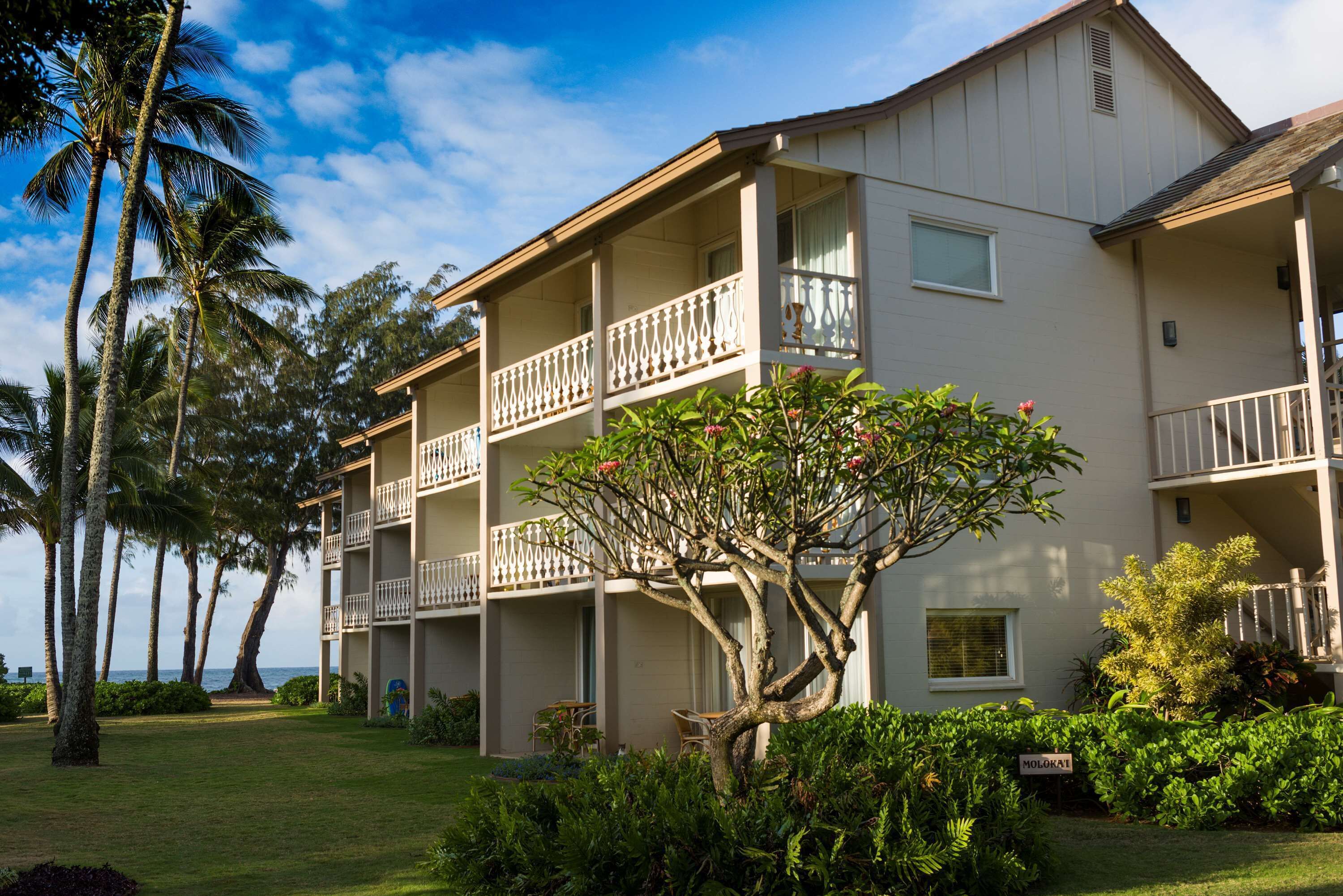 A multi-story hotel with balconies, a well-maintained lawn, and tropical vegetation.