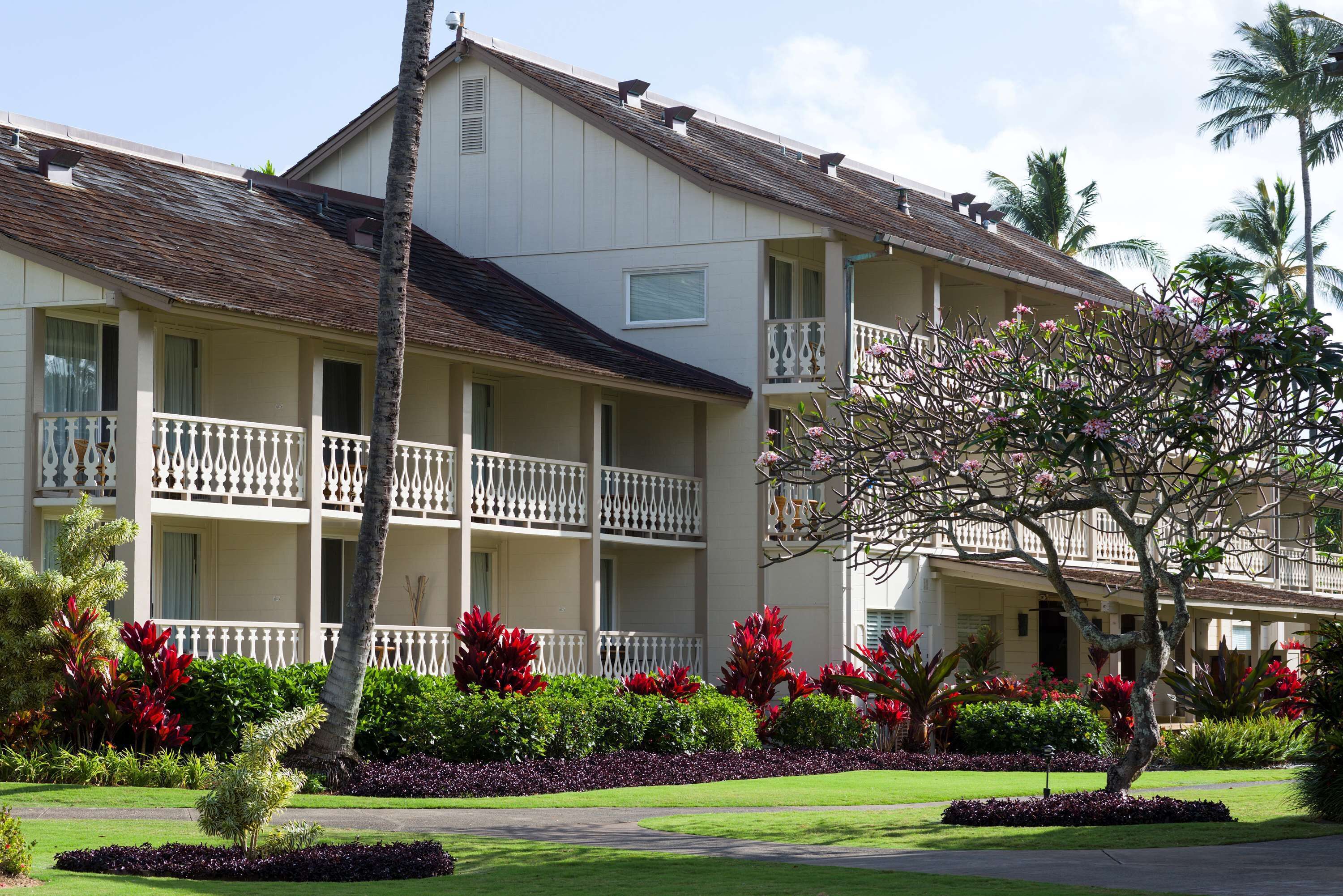 A multi-story hotel with balconies, surrounded by well-maintained gardens and palm trees.