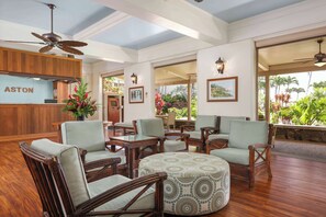 A spacious lobby with wooden furniture, a reception desk, and large windows offering a view of the outdoors.