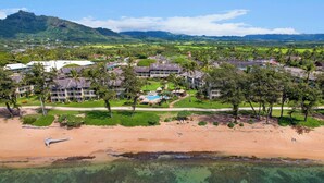 An aerial view of a resort with multiple buildings, a beach, and clear turquoise waters. - Aston Islander on the Beach (Kapaa)