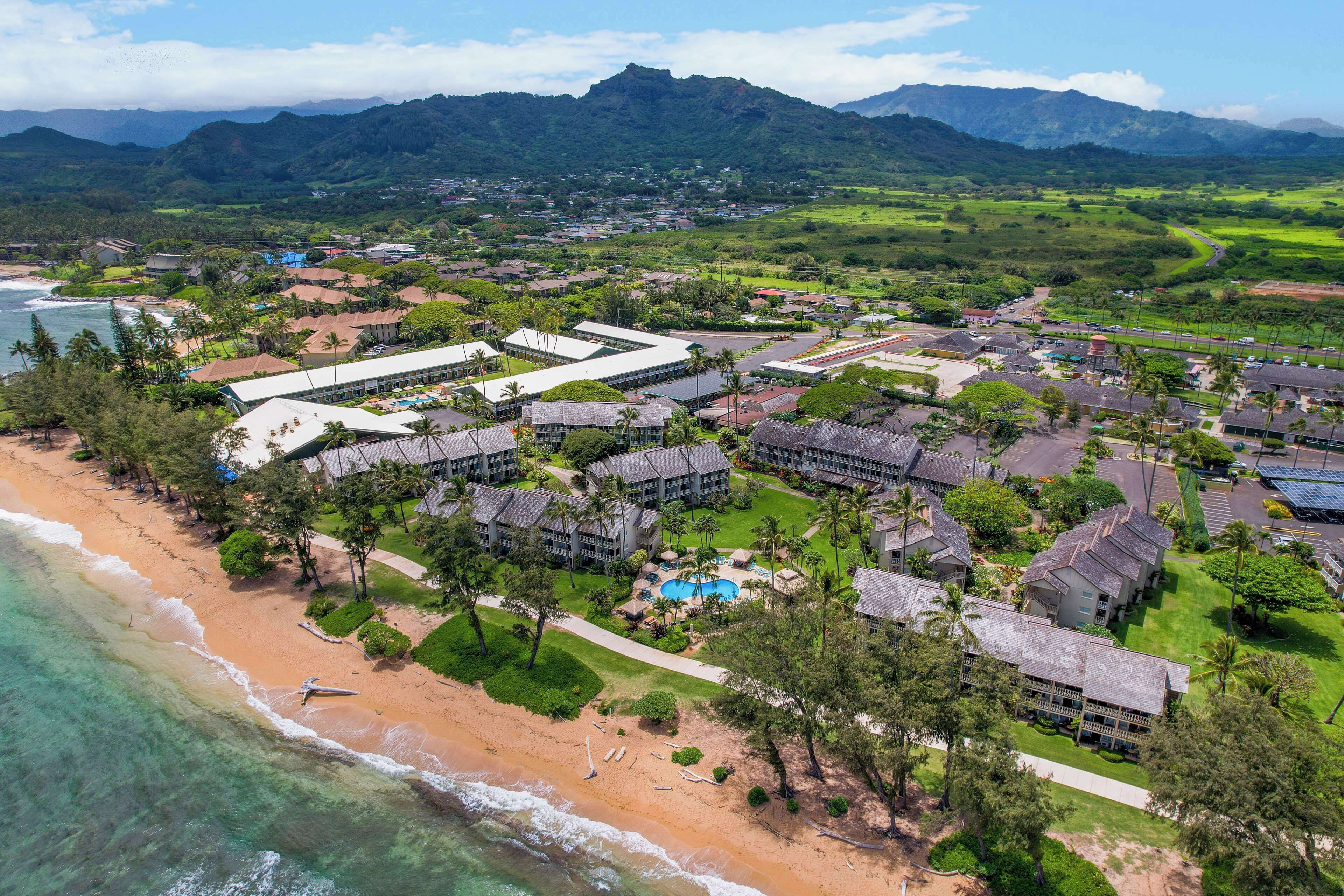 Vista aérea de un resort con propiedades frente a la playa, piscina y abundante vegetación.