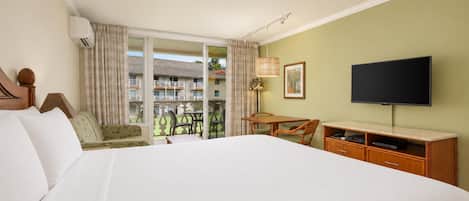 A hotel room with a large bed, a desk, a chair, a television, and a balcony with a view of other buildings.
