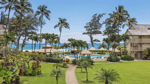A resort with a pool, palm trees, and a view of the ocean. - Aston Islander on the Beach (Kapaa)