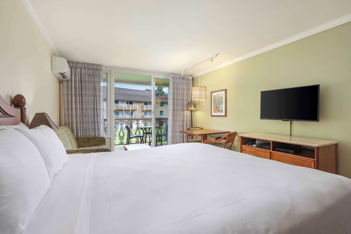Habitación de hotel con una cama grande, un escritorio con silla, televisión y balcón con mobiliario exterior.