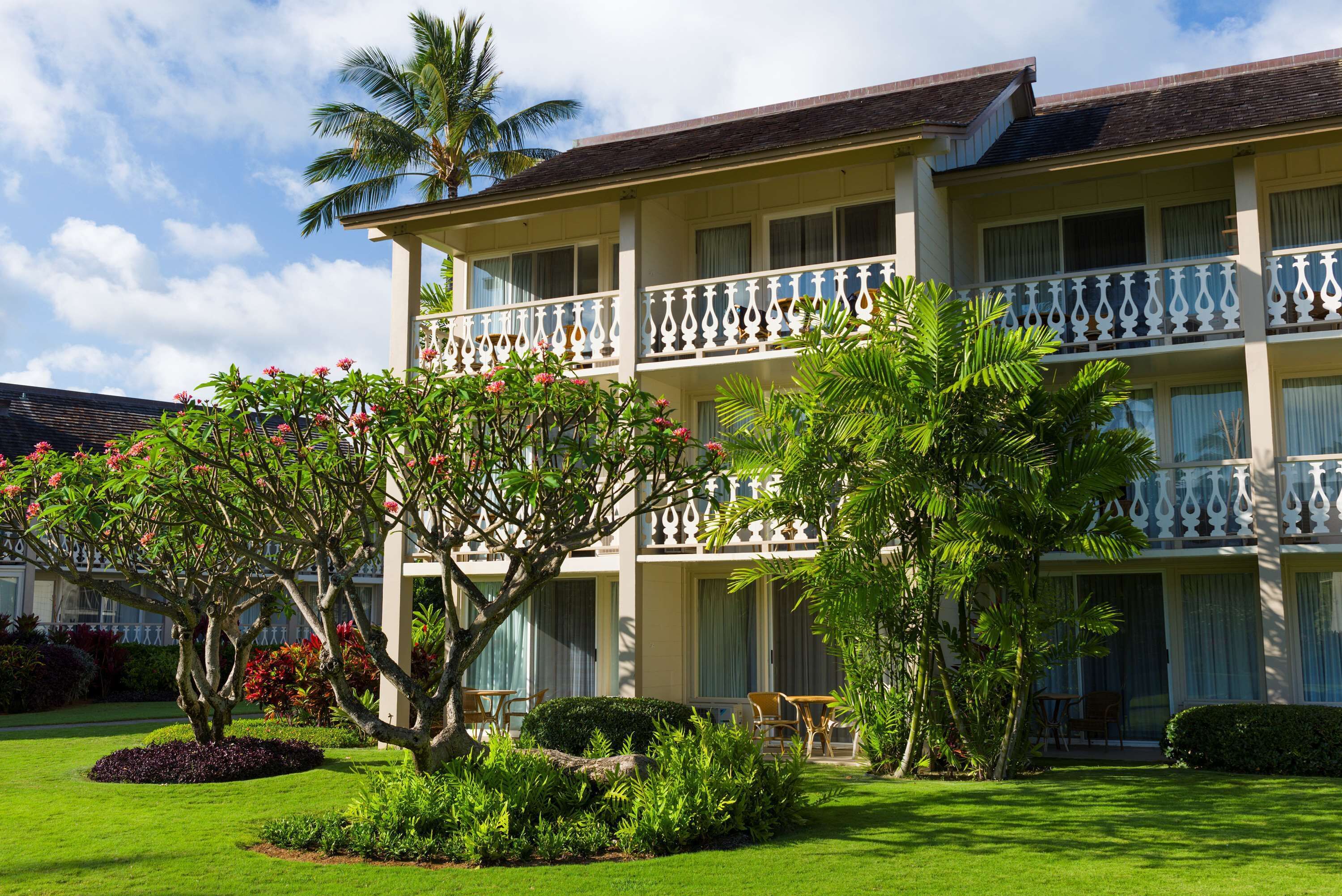 A multi-story hotel with balconies, lush greenery, and a well-maintained lawn.
