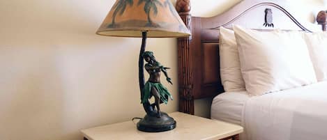 En seng med hvide sengetøj, et træhovedgærde og et natbord med lampe og statue.